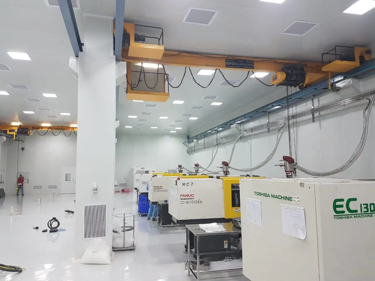 FANUC and Toshiba injection molding machines in a sterile cleanroom with an overhead gantry crane and white epoxy flooring.