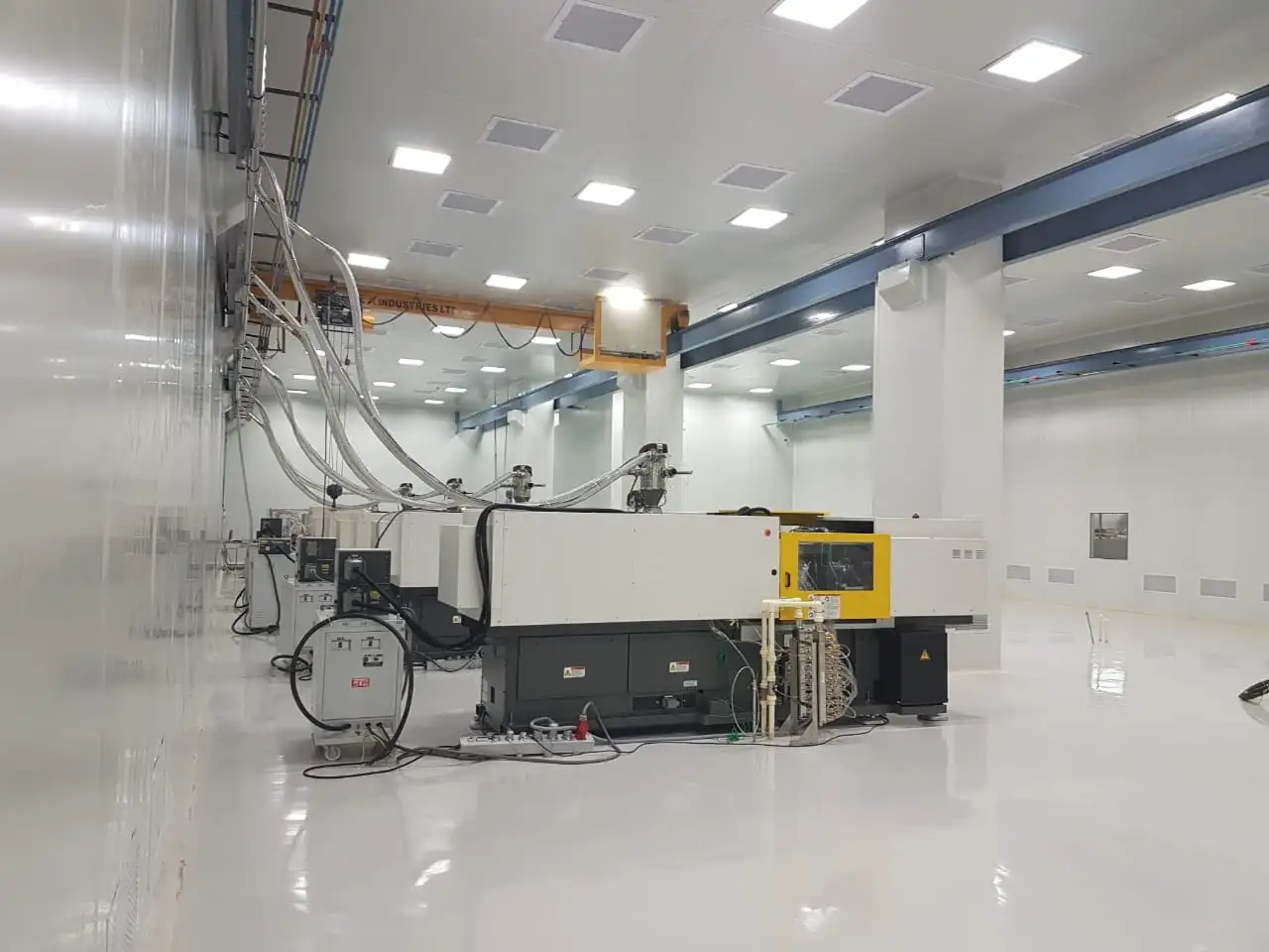 Side view of a Toshiba EC130 injection molding machine with material feed lines in a high-gloss cleanroom environment.