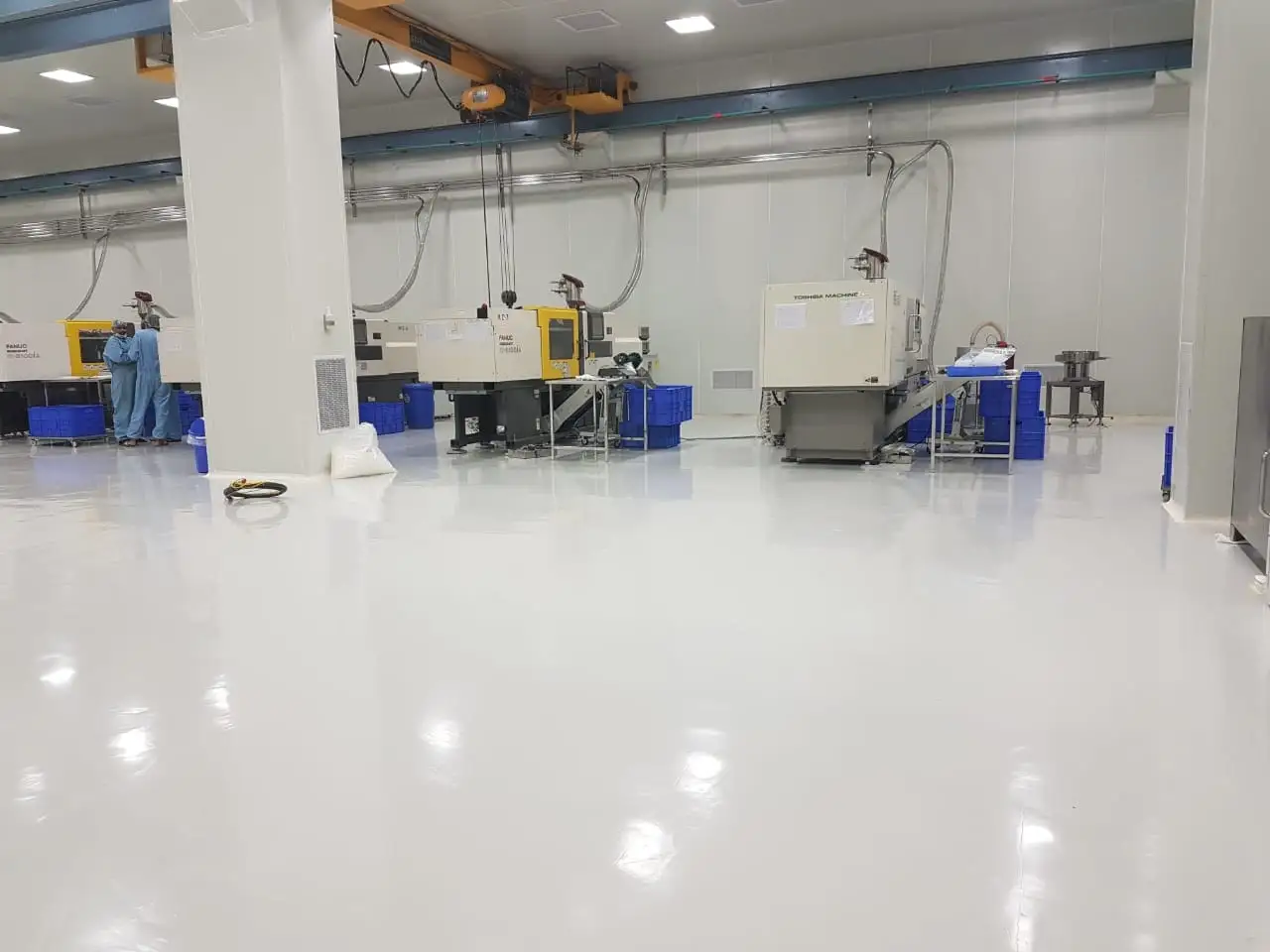 Technicians in sterile suits operating automated molding stations in a cleanroom manufacturing facility.