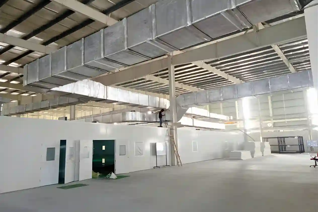 Large rectangular metal ventilation ducts suspended from the ceiling in a high-ceiling industrial facility.